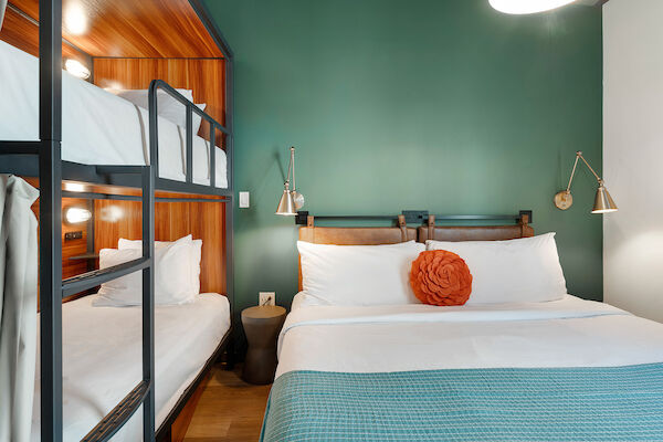 The image shows a well-decorated bedroom with a double bed, a set of bunk beds, green walls, and two wall-mounted bedside lamps.