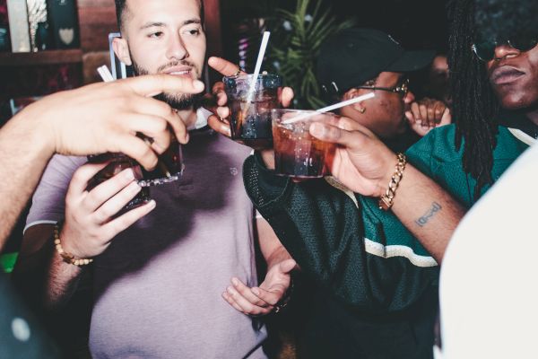 A group of people in a bar or club are raising their drinks for a toast, with a lively and social atmosphere in the background.