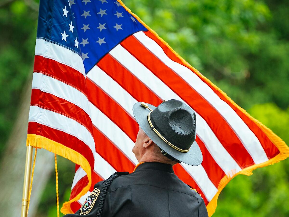 A person in uniform is holding a U.S. flag against a green, blurred background.